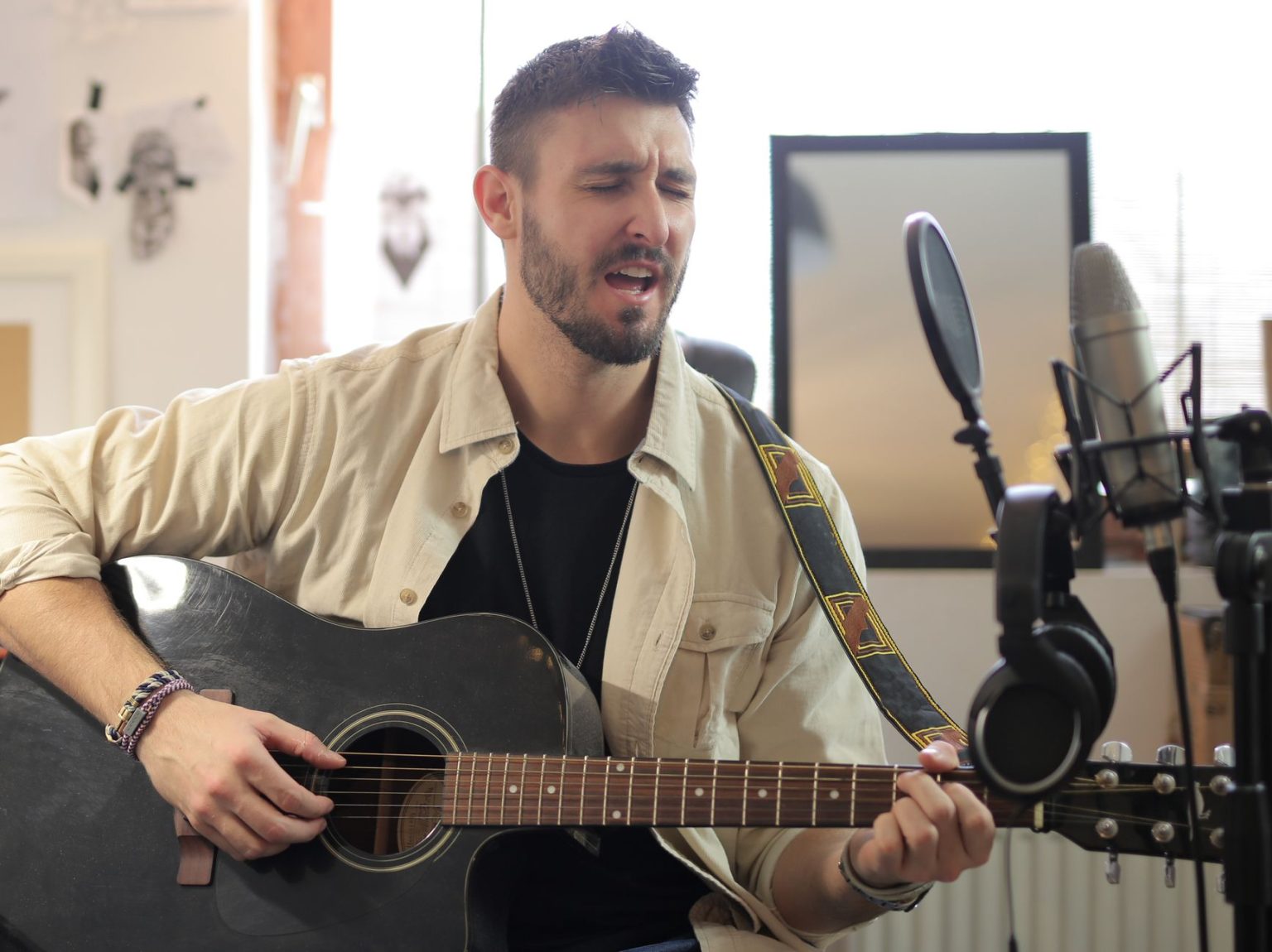 Músico canta e toca violão acústico em um estúdio de gravação.