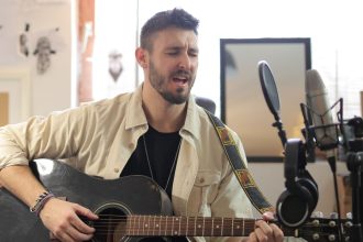 Músico canta e toca violão acústico em um estúdio de gravação.