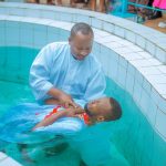 Pastor realiza batismo cristão em uma piscina diante de outra pessoa vestida de branco.