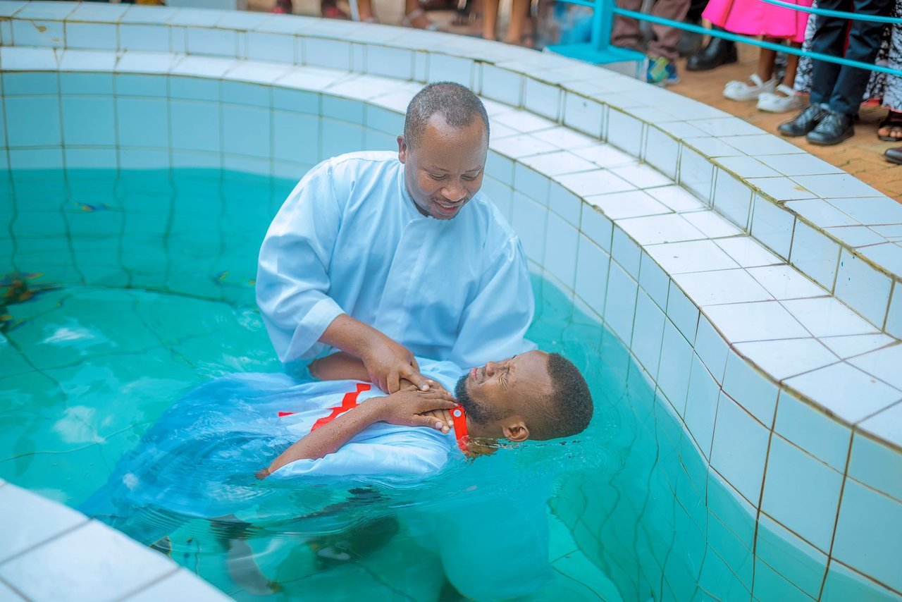 Pastor realiza batismo cristão em uma piscina diante de outra pessoa vestida de branco.