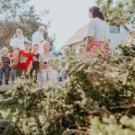Crianças e adultos participam de uma atividade educativa ao ar livre, cercados por vegetação.