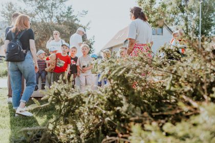 Crianças e adultos participam de uma atividade educativa ao ar livre, cercados por vegetação.